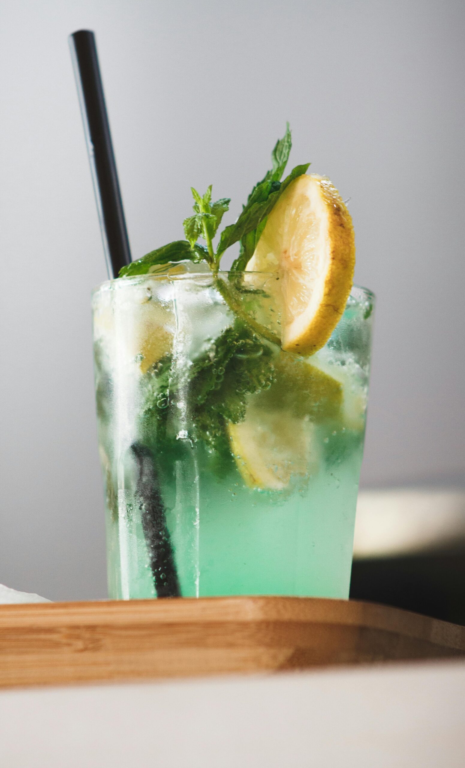 A vibrant mint mojito with fresh lemon wedge, ice, and mint garnish in a tall glass.